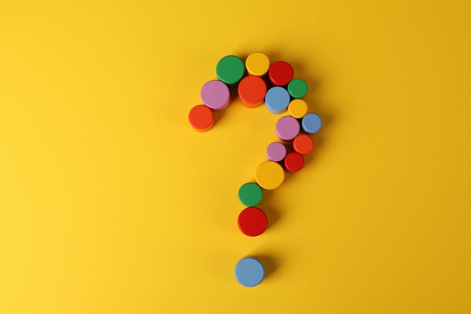 A vibrant question mark made from colorful circular blocks on a yellow background, symbolizing curiosity and inquiry.