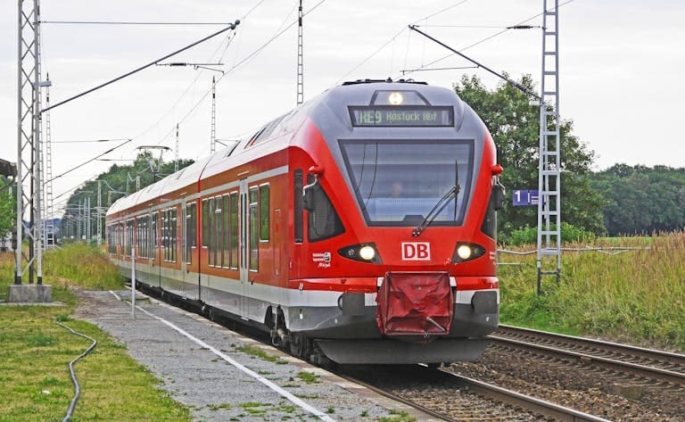 A vibrant red electric train arrives at a rural railway station, showcasing modern public transport.