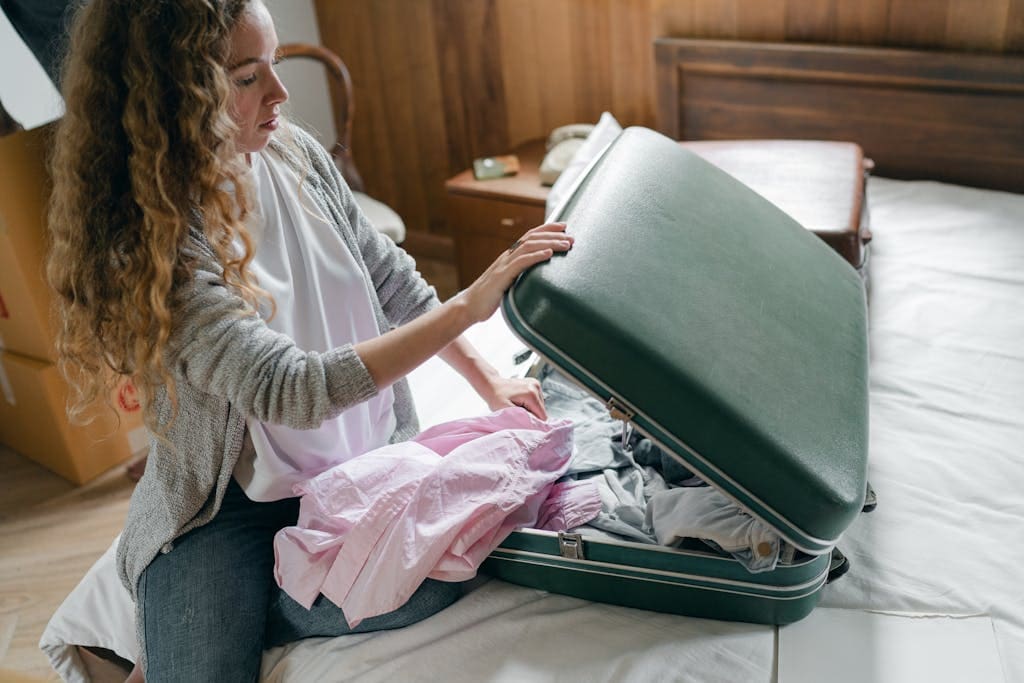 A young woman packing her suitcase in a bedroom, preparing for a journey.