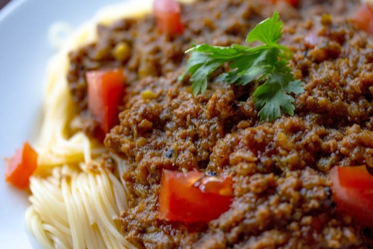 Close-up of a tasty spaghetti Bolognese topped with fresh parsley and tomatoes.