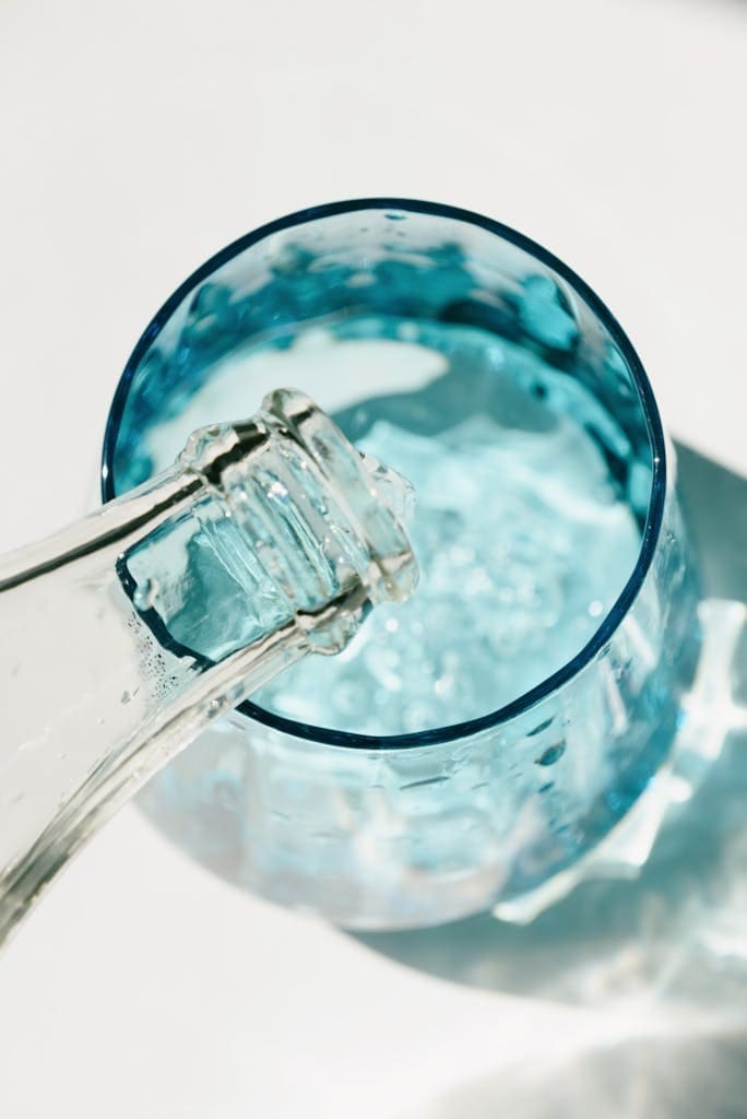 Close-up of water being poured into a blue glass in a sunny setting.