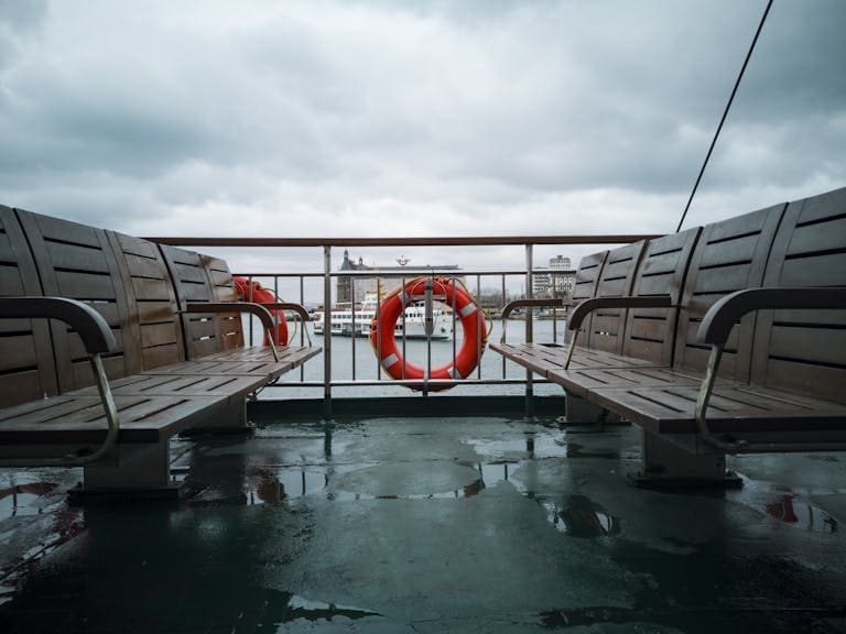 View from a ferry with wooden benches and lifebuoy on a rainy day.